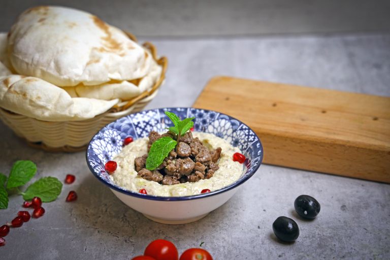 Delicious hummus bowl topped with meat and pomegranate seeds, served with fresh pita.