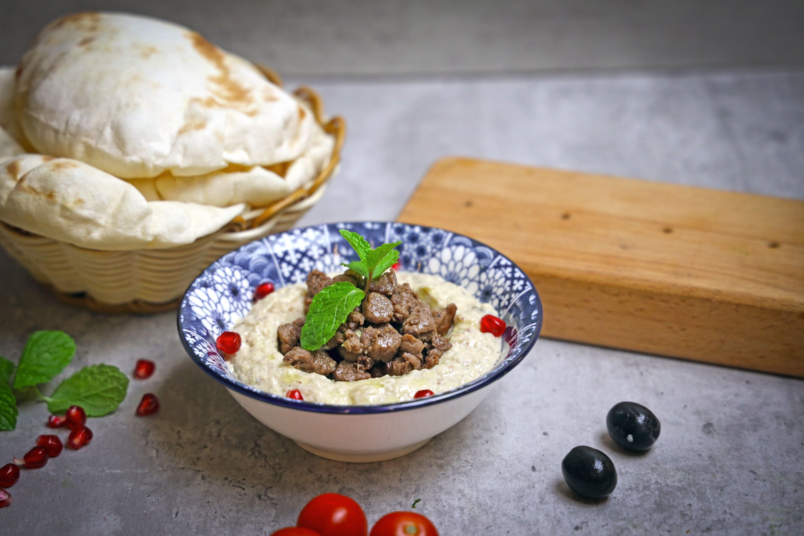 Delicious hummus bowl topped with meat and pomegranate seeds, served with fresh pita.