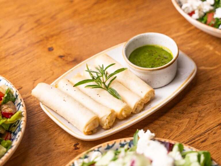 Appetizing vegetarian rolls served with herb sauce on a wooden table surrounded by salads.