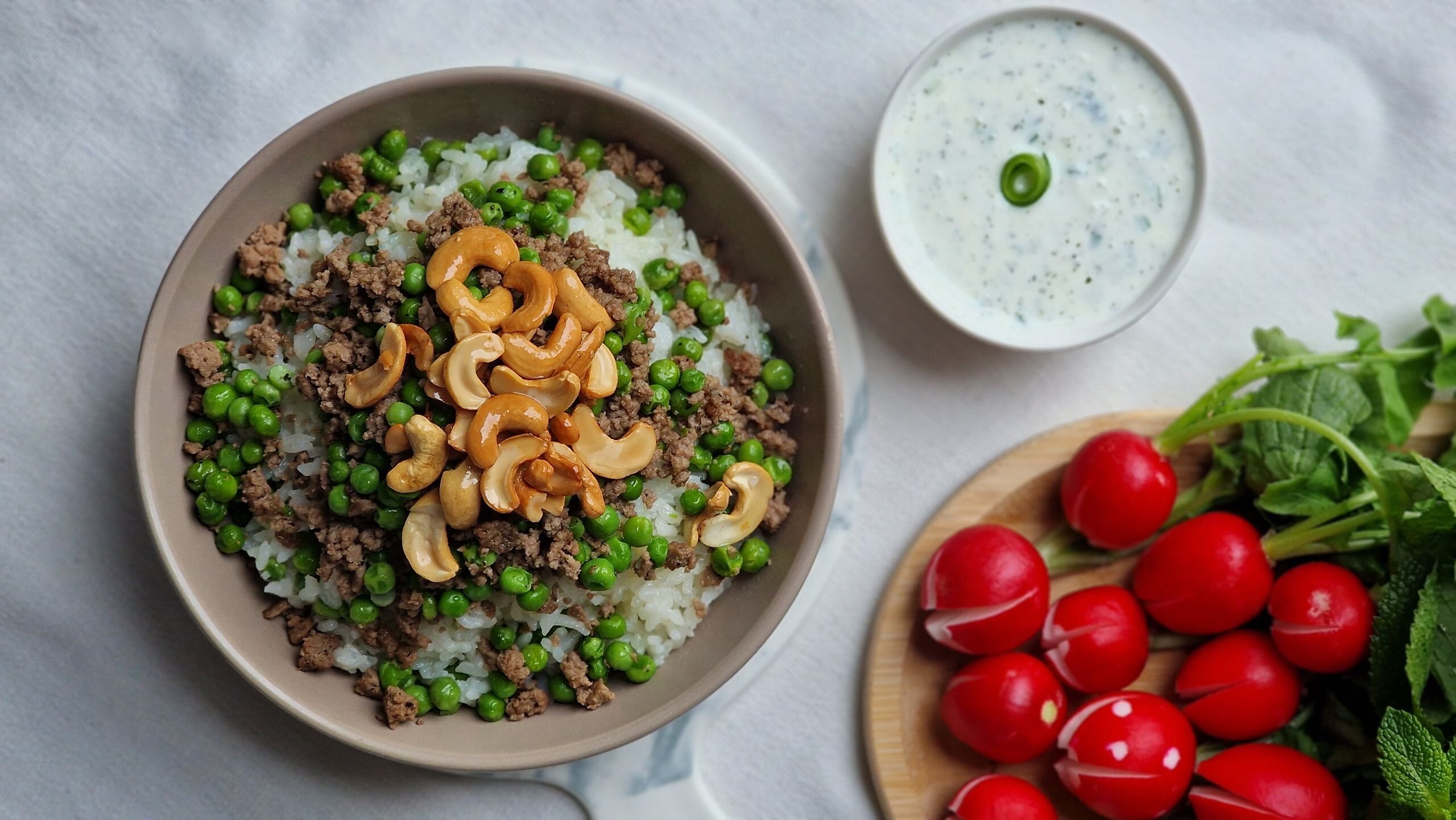 Rice with peas and cashews, served with fresh radishes and yogurt sauce for a nutritious meal.